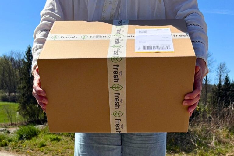 Verpacktes Gaumenfest-Paket in den Händen, bereit für den Versand regionaler Spezialitäten aus den Alpen